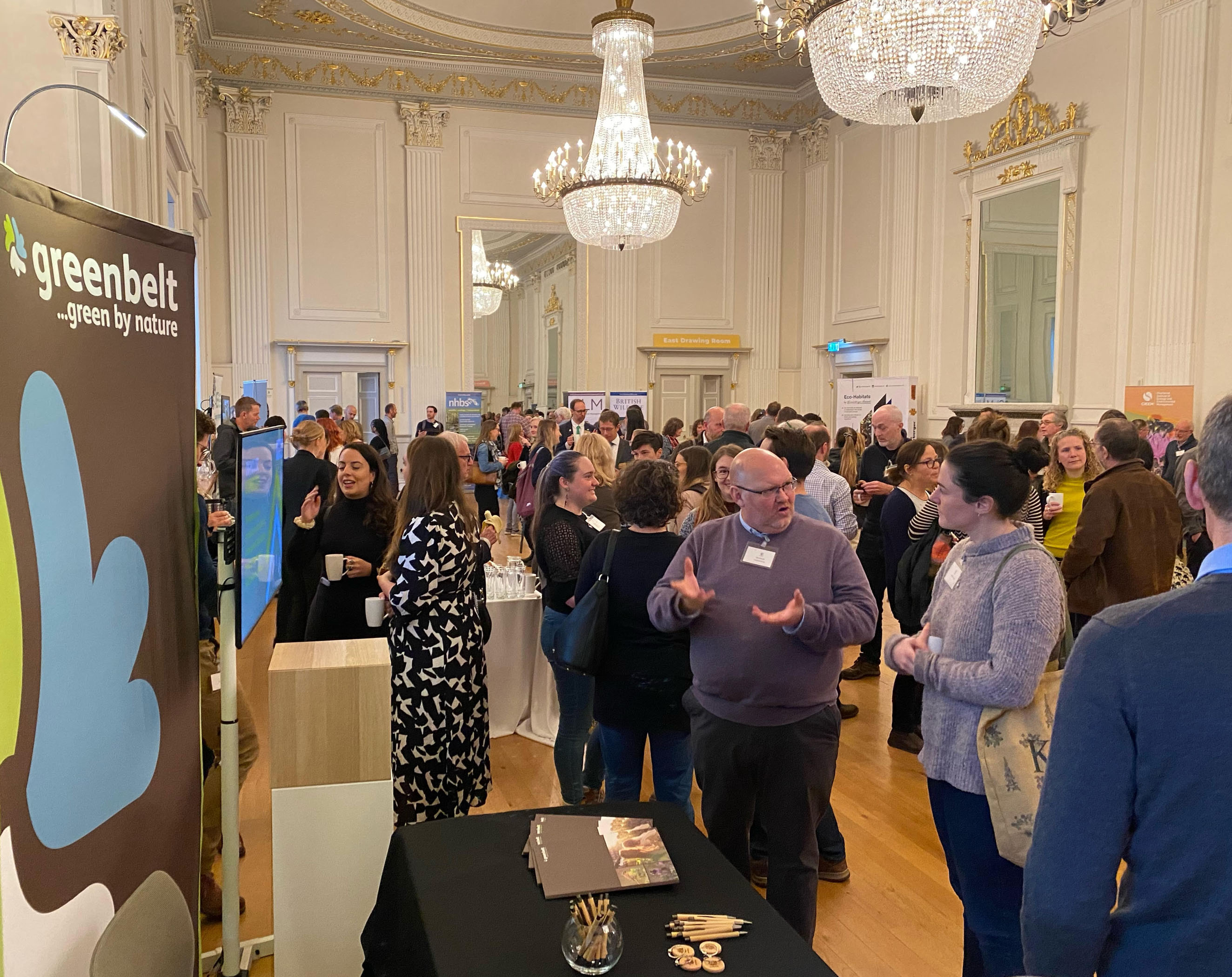 An image depicting Greenbelt staff manning a stall in a busy conference room
