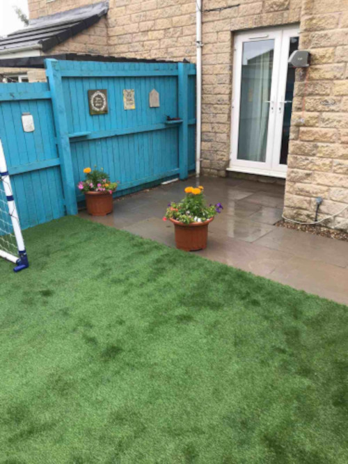 A residents backdoor with a blue painted fence and some potted plants on stone slabs