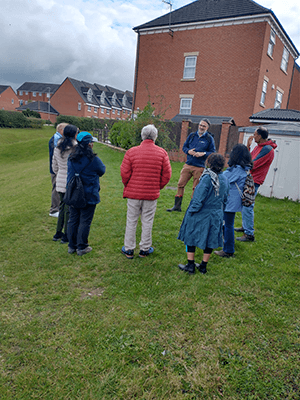A small group of homeowners gather outdoors to hear a talk regarding eco-friendly sustainable urban drainage