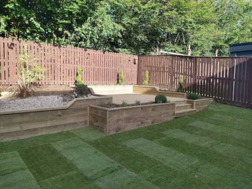 Wooden patteo with some stones and plants as decor inside a gated backgarden